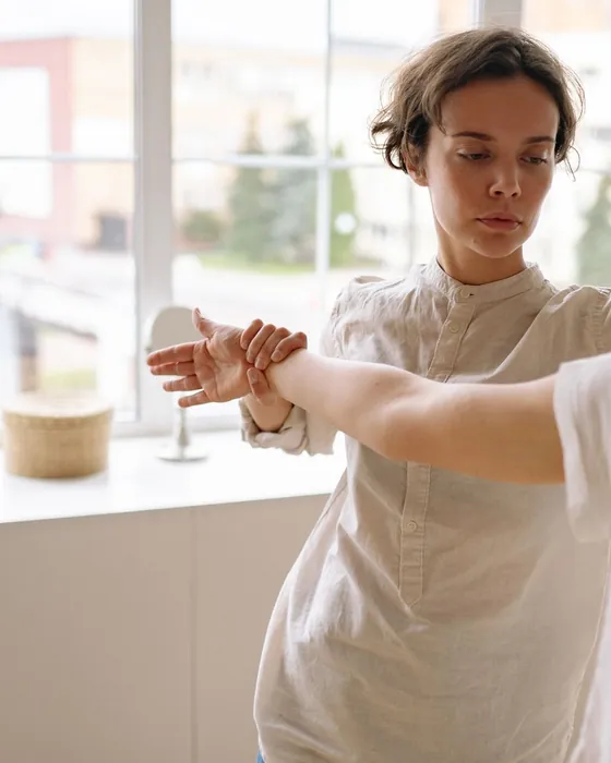 Elena Bassani accompagna con le mani il braccio teso di una persona, davanti a una finestra luminosa.